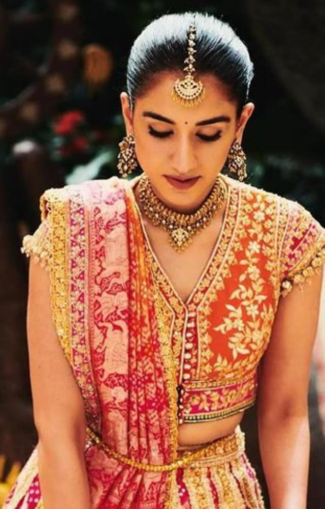 Radhika paired the heavy pink, orange, and gold lehenga with a statement neck piece, earrings, and a gold maang tika.
