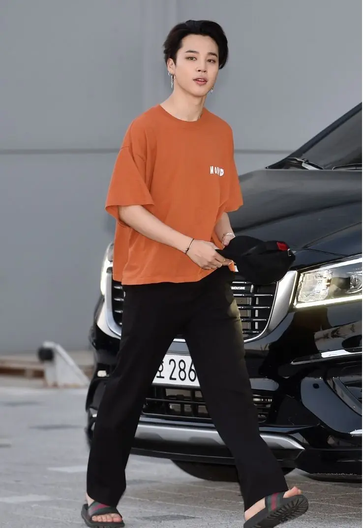 Jimin`s casual outfit of an orange t-shirt and black tracks is a testament to his laid-back style. It`s all about comfort without compromising on fashion.