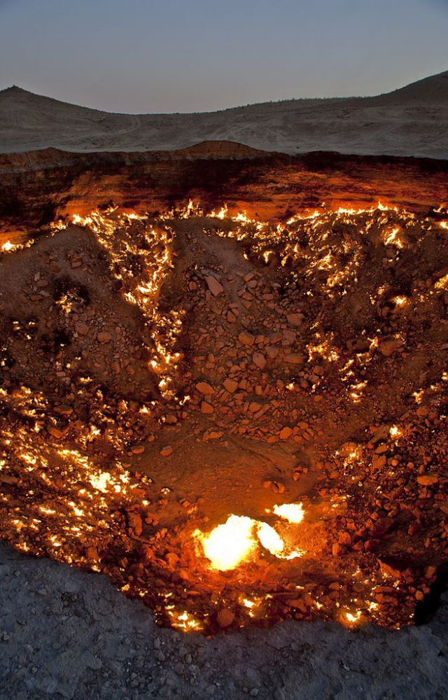 A burning 230-foot crater filled with fire and smoke—lit by geologists in 1971 and still alight, creating an inferno in the desert.
