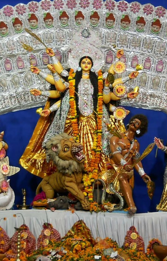 Place Durga’s idol with books on a shrine. Worship with vermilion, turmeric, and flowers, involving children in the ritual.