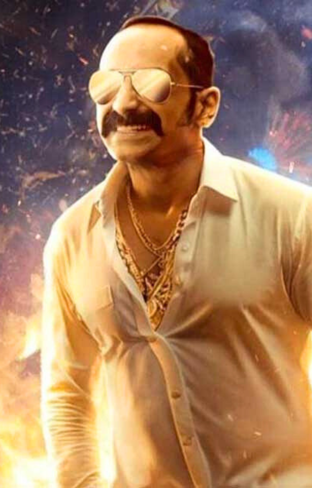 Ranga Annan dresses entirely in white, adorned with gold chains and rings. His signature sunglasses and unique attire make him stand out. 