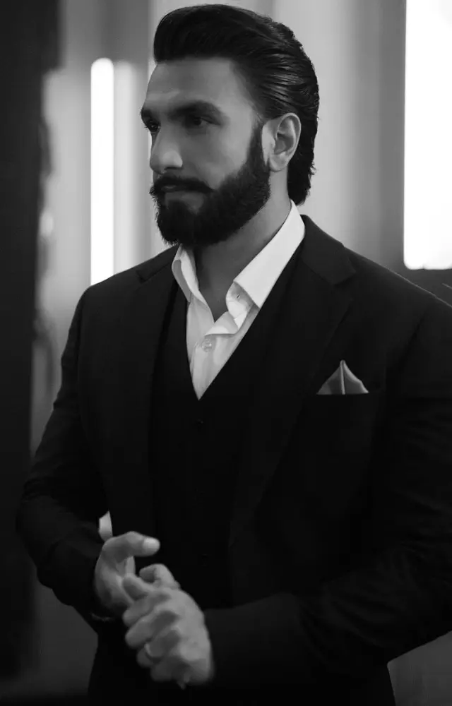 Ranveer effortlessly dons an ensemble comprising a black suit layered over a white shirt, tucked neatly