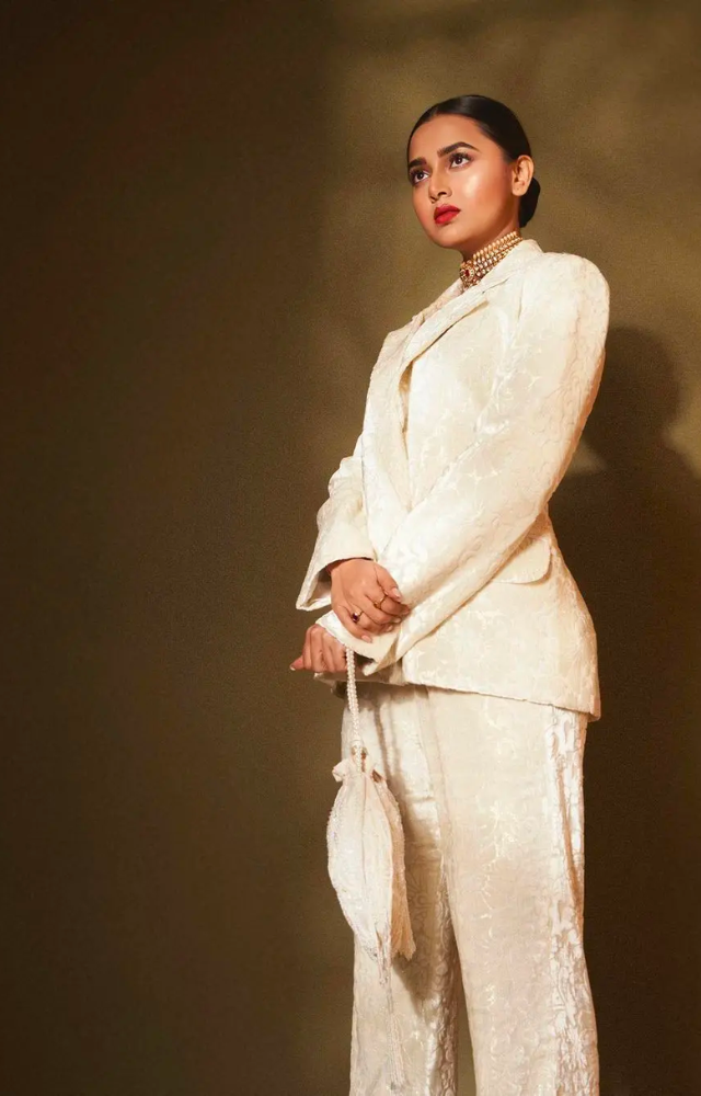  Completing the look, she adds an off-white flower in her hair and a stylish golden close-necked necklace, elevating the overall glamour of her attire.