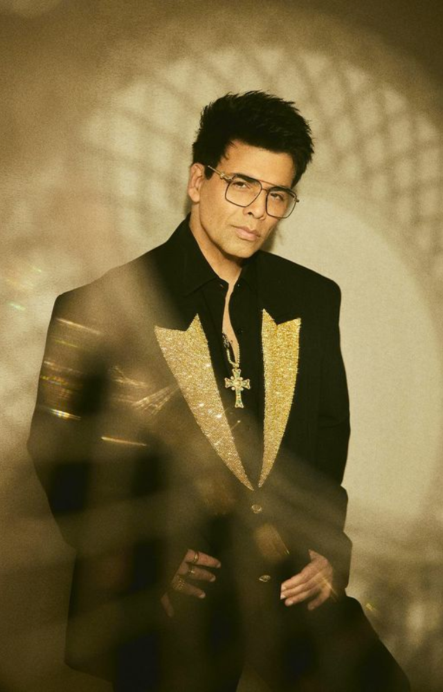 Karan Johar radiates style brilliance in a black-gold blazer, accentuated by a Jesus cross, creating a stunning fashion statement.