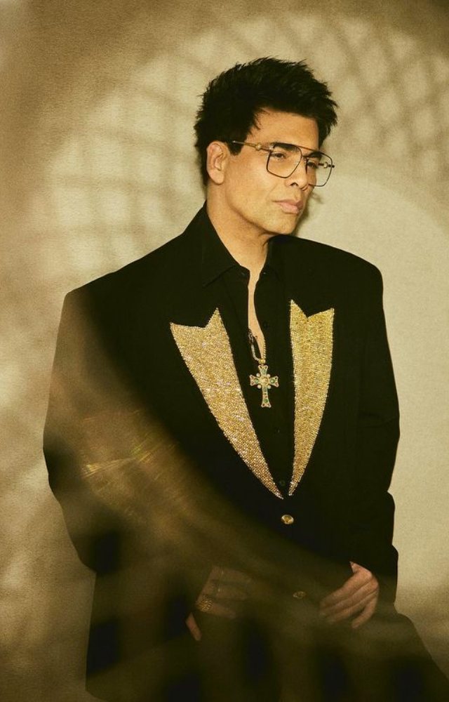 Embracing sophistication, Karan Johar dazzles in a black-gold blazer, complemented by a Jesus cross, showcasing refined fashion flair.