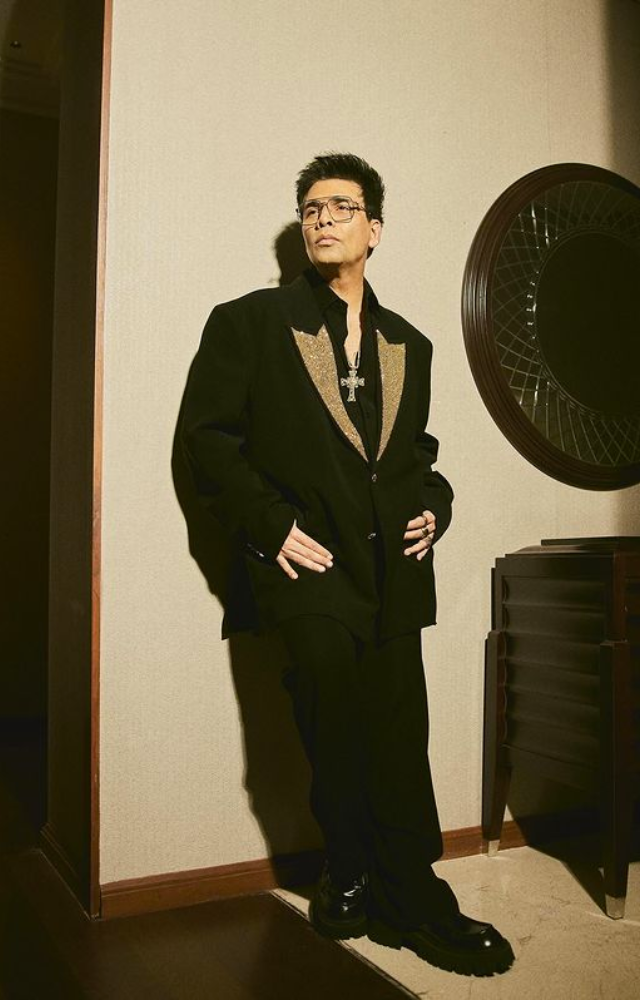 Karan Johar shines in a captivating black-gold blazer, adorned with a Jesus cross, exuding elegance and divine style.