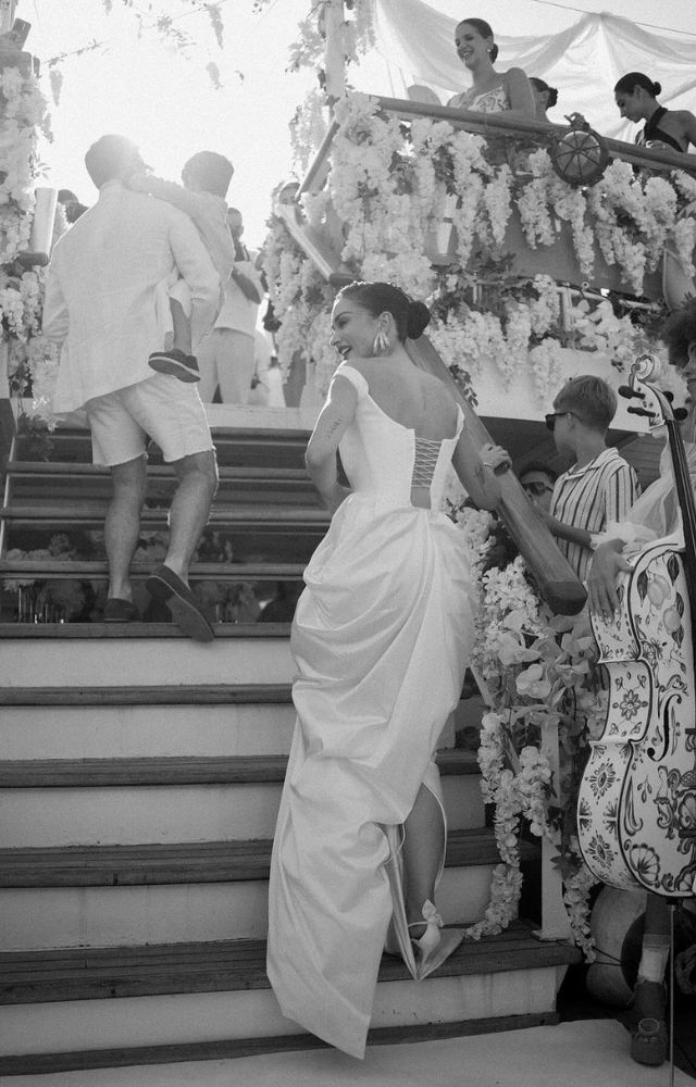 Amy Jackson dazzles in a stunning white gown, with an elegant smile on her face, surrounded by floral arrangements.
