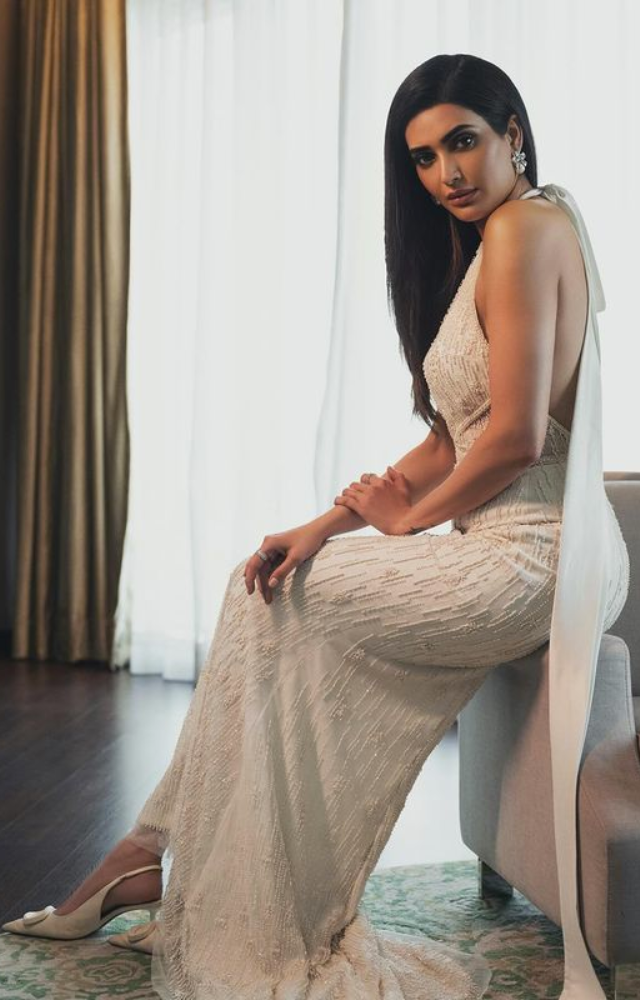 Karishma Tanna strikes a pose on a sofa in a white gown at Filmfare, exuding glamour and sophistication, creating a captivating and stylish image.