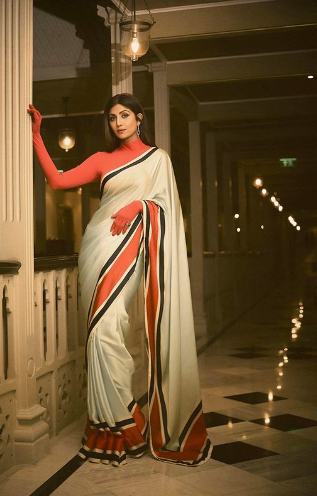 Shilpa Shetty enters the scene sporting an exquisite red-white saree, exhibiting the ideal fusion of style, grace, and feminine charm.